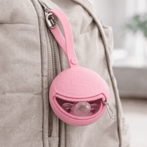 Pink silicone pacifier holder attached to backpack with secure zipper and clip
